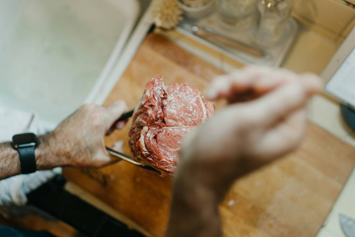 person holding raw meat on brown wooden chopping board